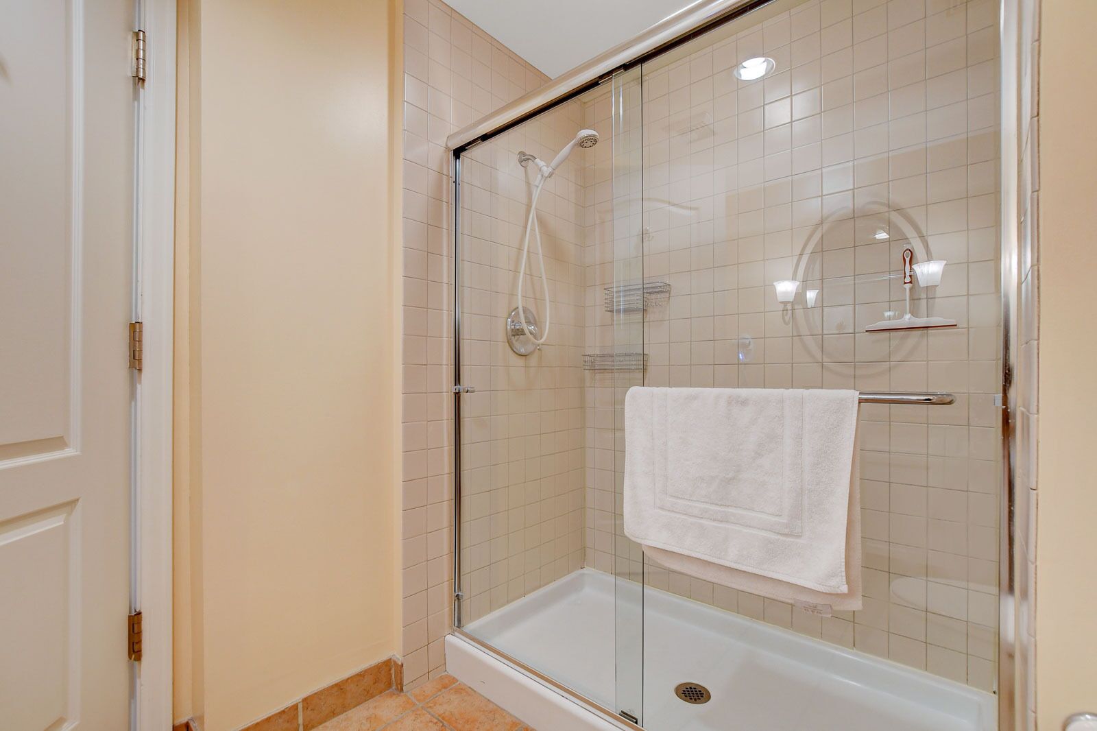 Une douche en verre avec une porte en verre, une serviette blanche accrochée à la porte et une baignoire avec un drain.