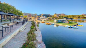 A waterfront area with a dock, boats, and a row of outdoor seating along the water's edge. - OVER-SIZED 2 BR PATIO UNIT STEPS TO POOL & COURTYARD!!! (Henderson)