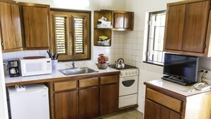 Una cocina compacta con armarios de madera, microondas, estufa, lavaplatos y televisor.