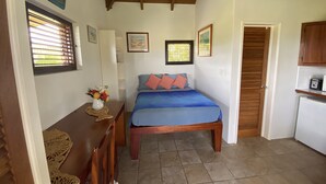 Un dormitorio con cama, escritorio con un florero, puerta de madera y kitchenette.