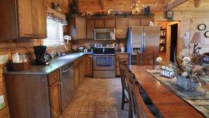 A wooden cabin kitchen with a central island, stainless steel appliances, and a dining area with wooden chairs. - Timber Mountain Lodge,  Private Hot Tub .1 Mi to Thunder Ridge; 10 min Branson  (Ridgedale)