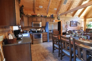 A wooden cabin interior with a kitchen featuring stainless steel appliances, a dining area with a table and chairs, and a cozy fireplace.