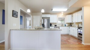Uma cozinha moderna com ilha central, armários brancos, eletrodomésticos de aço inoxidável e iluminação pendente.