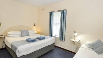 A hotel room with a bed, bedside tables, a window with curtains, and a wall-mounted light fixture.