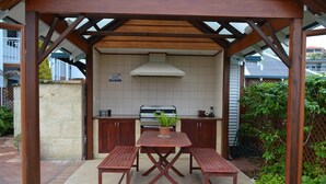 Un'area cucina esterna con barbecue, tavolo e panche, e una struttura a pergola.