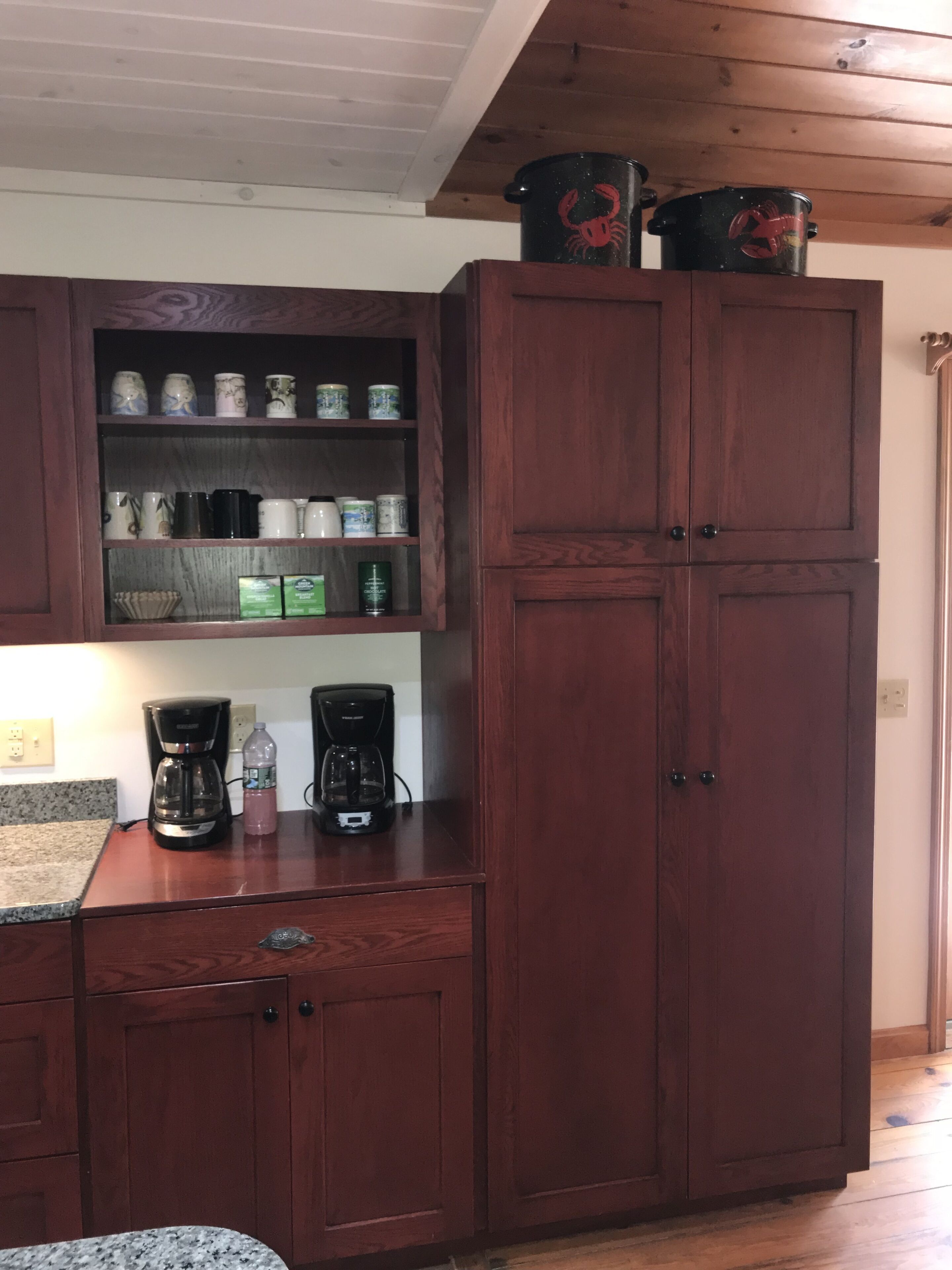 Ein Holzkasten mit Regalen, der verschiedene Küchenutensilien, eine Kaffeemaschine und eine Wasserflasche auf einer Arbeitsplatte beherbergt.