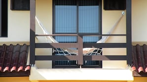 Ein Balkon mit Hängematte, ein Fenster mit Jalousien und ein Ziegeldach.