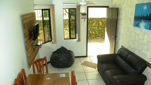 A living room with a wooden dining table, a black bean bag, a leather sofa, and a television on the wall. - Great two-story house 150 meters from the beach. Summer 2026 with incredible prices! (Bombinhas)