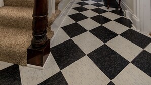 Ein Flur mit Schachbrettfußboden in Schwarz und Weiß, einer Holztreppe mit Geländer und einer Tür am Ende.