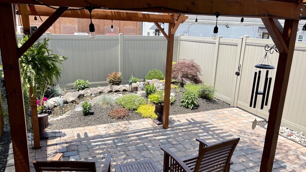Eine Holz-Pergola mit Pflasterterrasse, zwei Holzstühlen und einem kleinen Tisch.