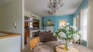 Ein Essbereich mit rundem Tisch, Stühlen und einer Chandelüster. Im Hintergrund ist eine Küche mit Holzausbau und einer weißen Arbeitsplatte zu sehen.