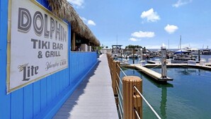A dock with a sign for 'DOLPHIN TIKI BAR & GRILL' and a view of a marina with boats. - Great Unit On Marco River (marco island)