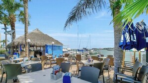 An outdoor dining area with tables and chairs, a thatched-roof structure, and a view of the marina. - Great Unit On Marco River (marco island)