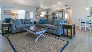 A modern living room with a grey sectional sofa, a coffee table, and a dining area with a white table and chairs.