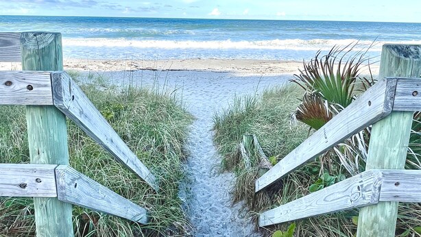 A wooden pathway leading to a beach with a clear view of the ocean.