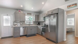 A modern kitchen with grey cabinets, stainless steel appliances, and a wooden floor.