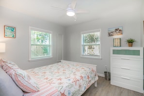 A bedroom with a bed, a dresser, and two windows with blinds.
