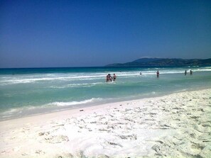 A beach with clear blue water, sandy shore, and a distant mountain.