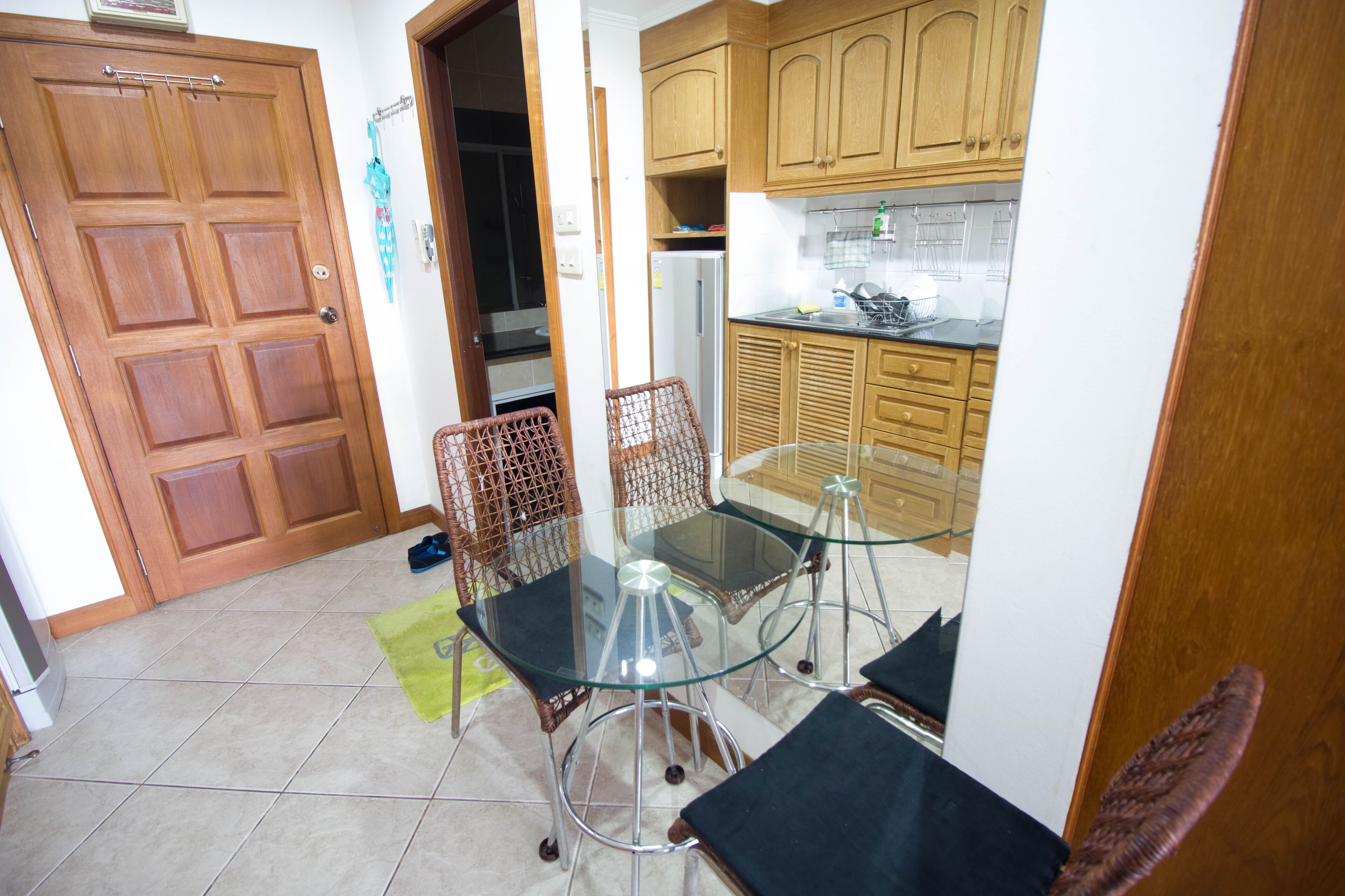 A compact kitchen with wooden cabinets, a glass-top dining table, and wicker chairs.