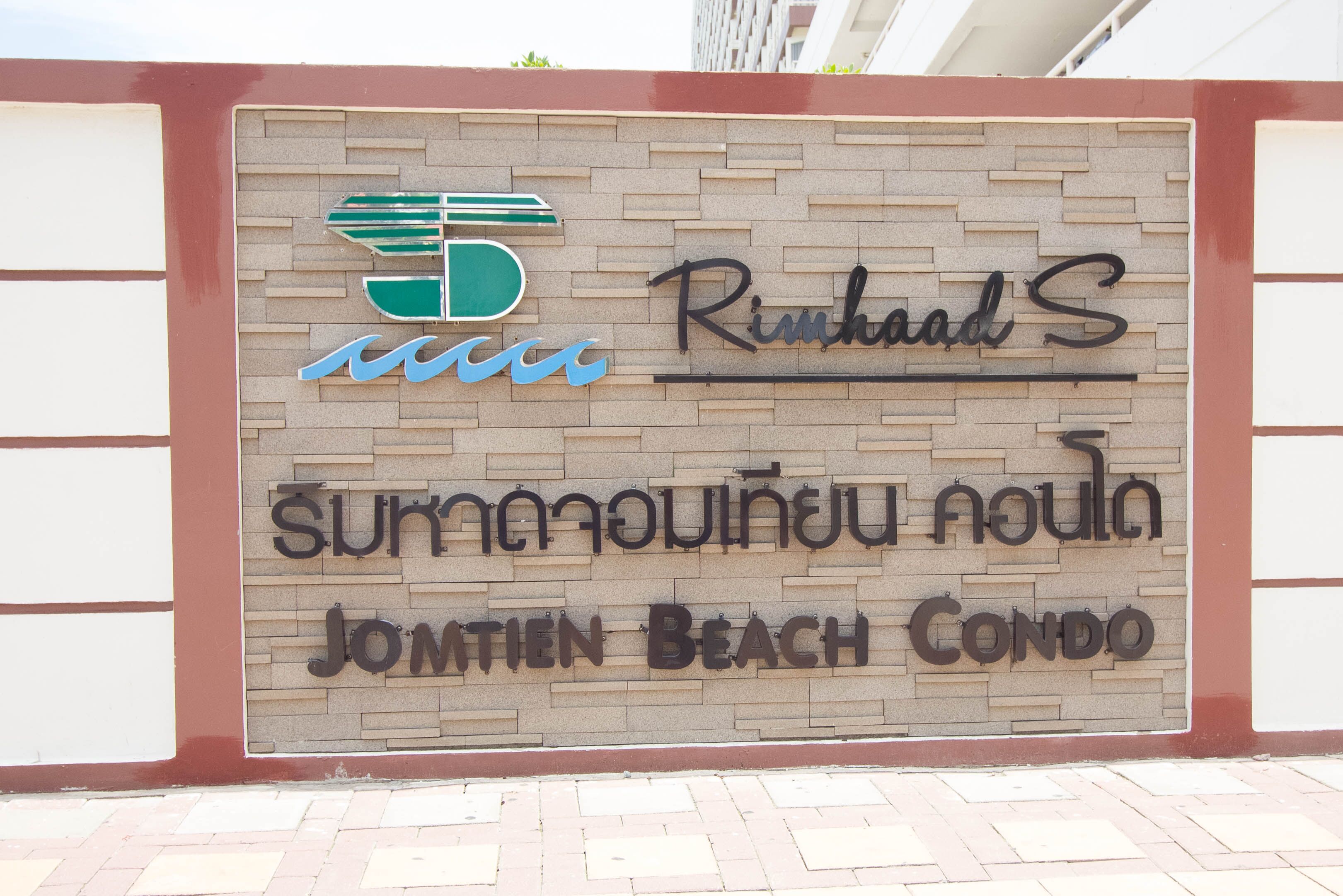 Une enseigne pour le complexe d’appartements Jomtien Beach, avec un logo et un texte en plusieurs langues.