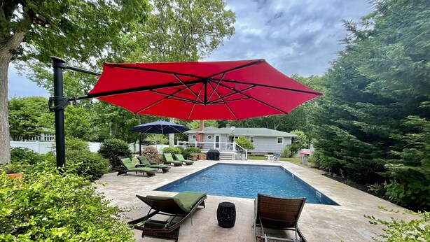 Une piscine avec des chaises longues et un parasol rouge.