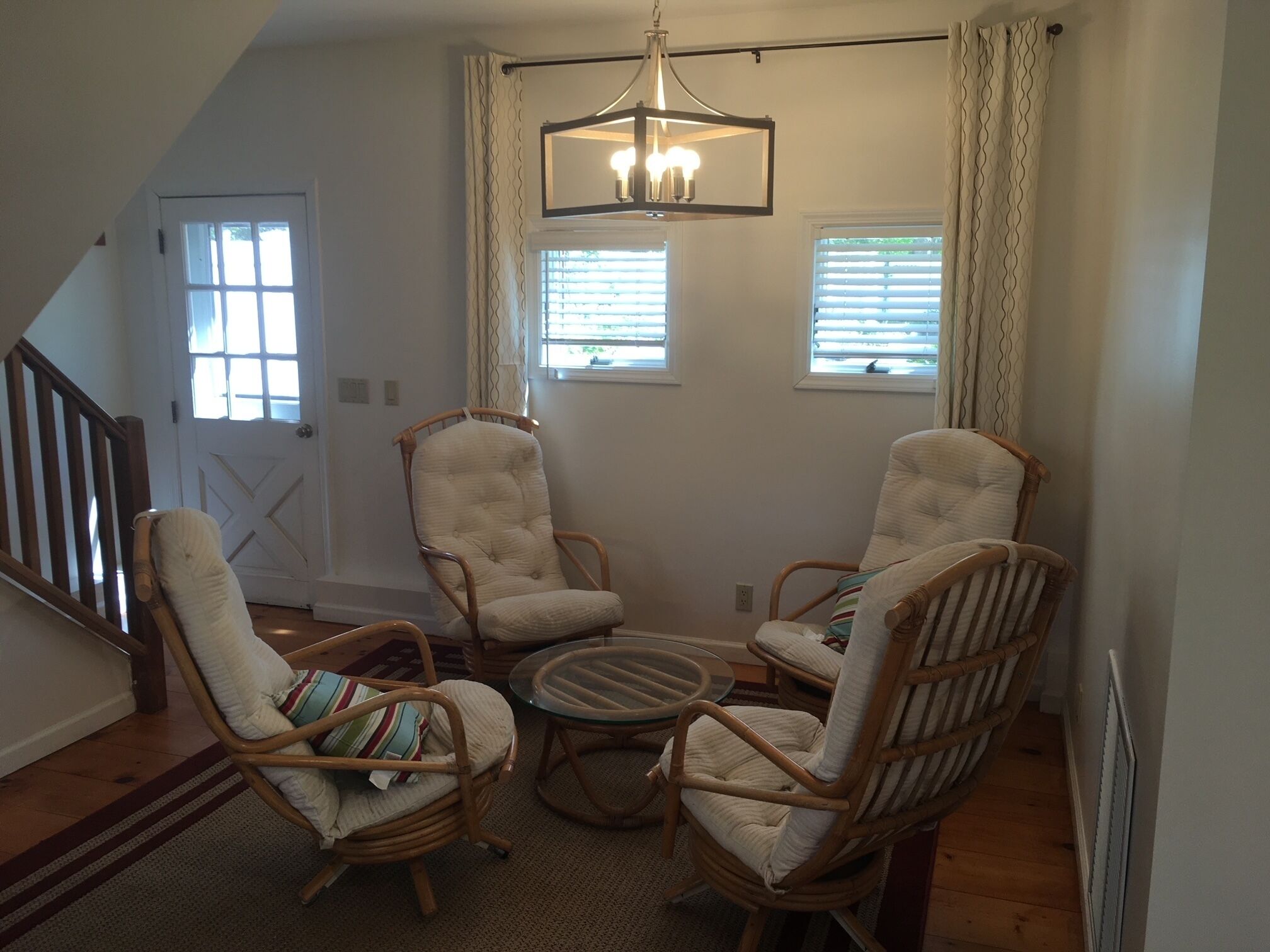 A living room with three wicker chairs, a glass coffee table, and a hanging light fixture.