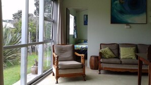 Een woonkamer met een groot raam, een houten stoel, een bank en een schilderij aan de muur.