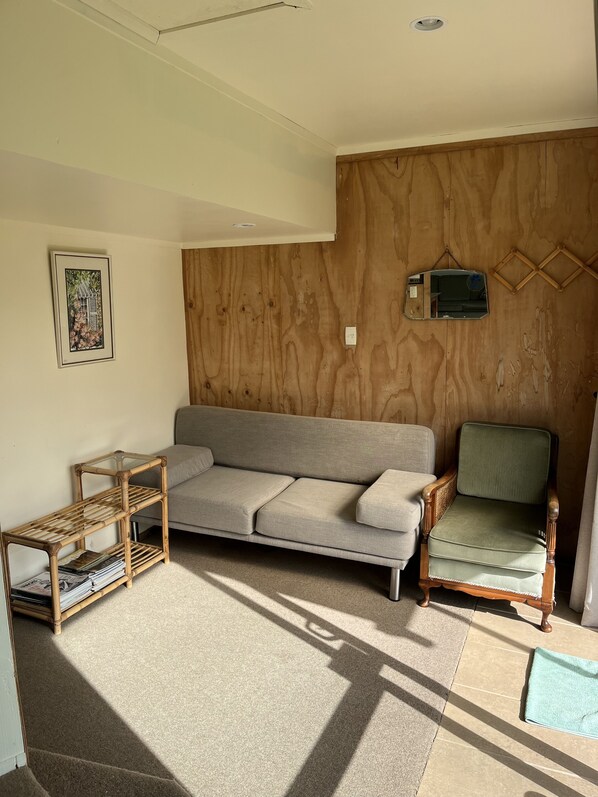 A living room with a sofa, a chair, a small table, and a wall-mounted shelf. - SANDY BAY - Sublime beachside (Sandy Bay (Tutukaka Coast))