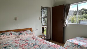 Een slaapkamer met een bed, nachtkastje, raam met gordijnen en uitzicht op groen.