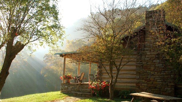A rustic log cabin with a stone foundation, a covered porch with chairs, and a picnic table. - It's a place that attracts happiness. (Lexington)