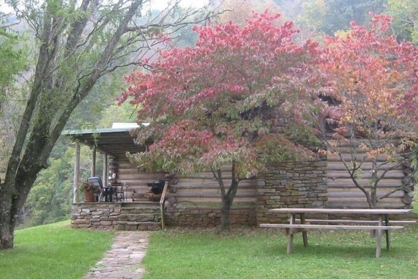 Una cabana rústica de fusta amb façana de pedra, un porxo cobert amb seients exteriors i una taula de pícnic.