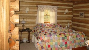 A log cabin bedroom with a quilted bedspread, a bedside lamp, and a window with a butterfly-shaped stained glass. - It's a place that attracts happiness. (Lexington)