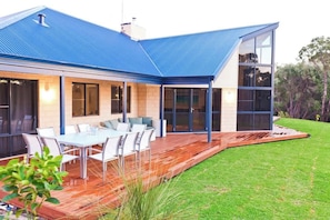 A modern house with a blue roof, large windows, and a deck with outdoor furniture.