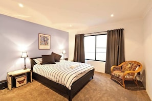 A bedroom with a bed, bedside lamps, a chair, a window with curtains, and a wall-mounted picture.