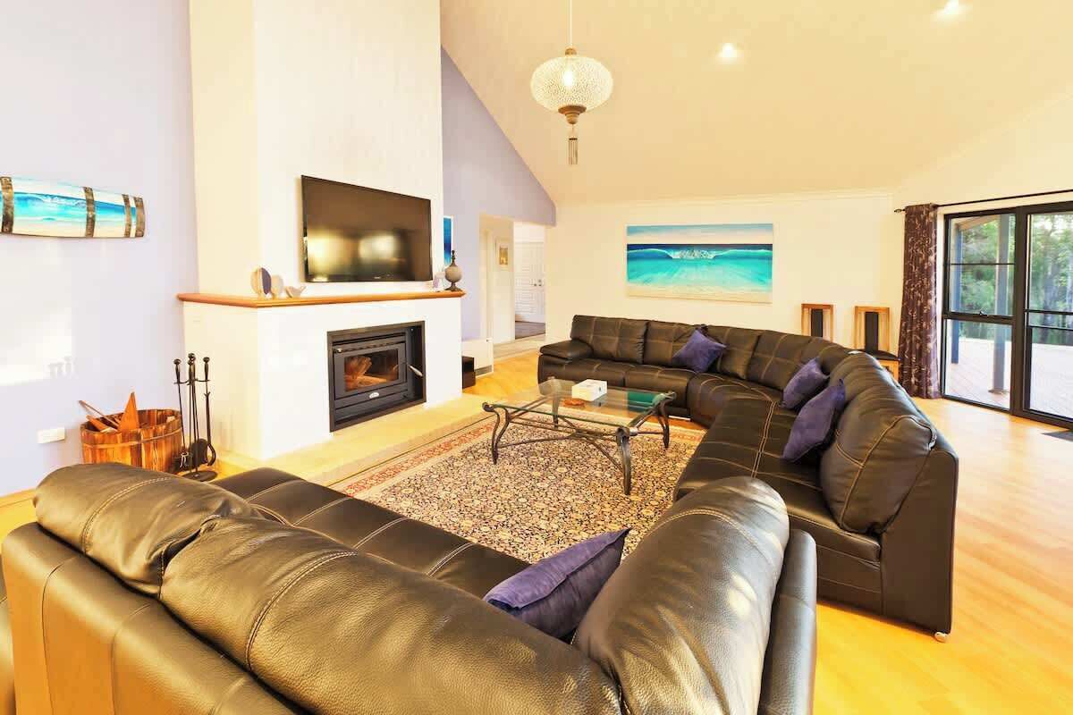 A modern living room with a fireplace, leather sofas, a flat-screen TV, and a large window with a view.