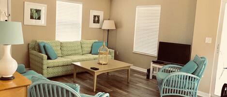 A living room with a sofa, two chairs, a coffee table, a TV, and a ceiling fan.
