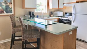 A kitchen with a glass island, wooden cabinets, a microwave, stove, and a refrigerator. - Cudjoe Cottages, swimming pool, just 20 miles from Key West (Cudjoe Key)