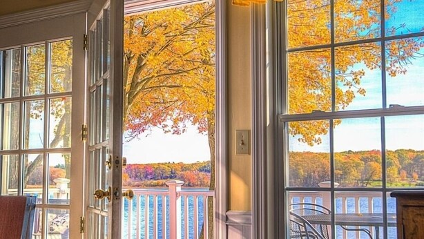 Ein Zimmer mit einem großen Fenster, einer zur Außenwelt führenden Tür und Blick auf eine Terrasse mit Geländer.