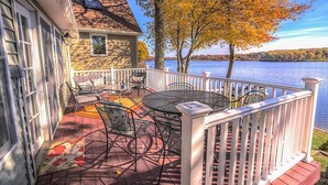 Eine Terrasse mit Gartenmöbeln, einem Geländer und Blick auf einen See.