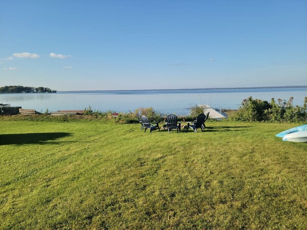 A grassy area with chairs and kayaks by a lake.