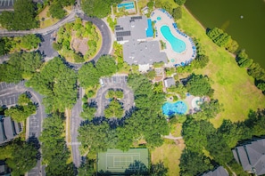 Vista aérea de una propiedad con piscina, cancha de tenis y vegetación circundante.