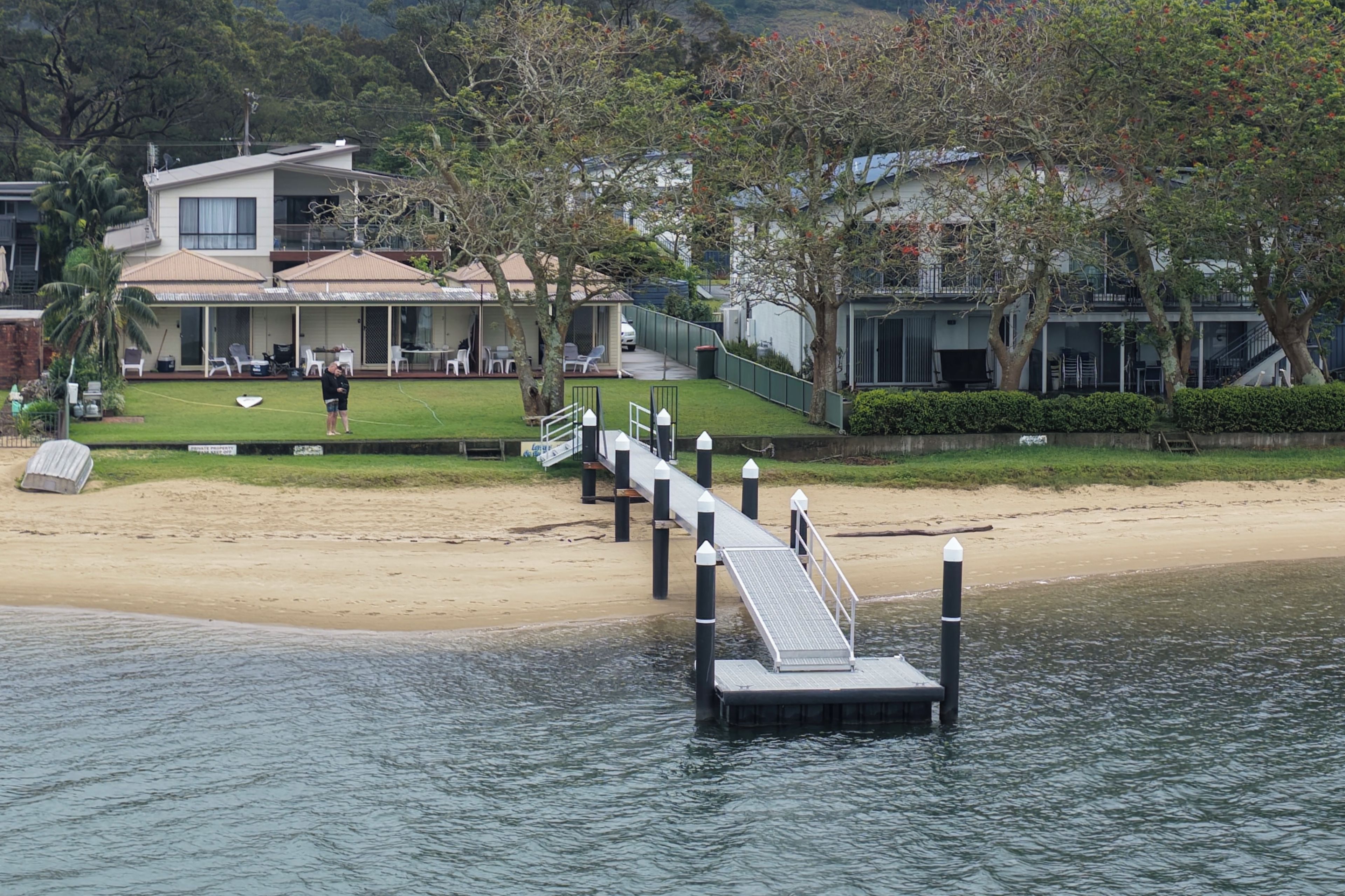 A waterfront property with a dock leading to a beach, a covered patio area, and a building with a modern design.