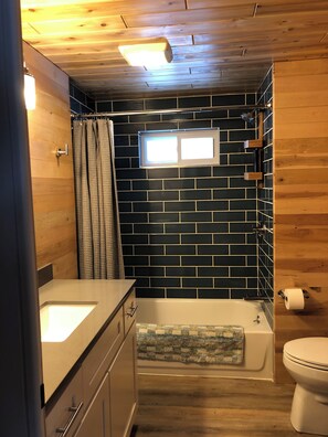 Une salle de bain avec un plafond en bois, une baignoire, des toilettes, une fenêtre et un porte-serviettes.