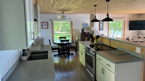Une cuisine avec un plafond en bois, un coin repas avec des chaises, une cuisinière et un téléviseur fixé au mur.