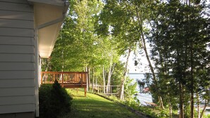 Une terrasse en bois avec un banc, une zone herbeuse et une étendue d’eau en arrière-plan.