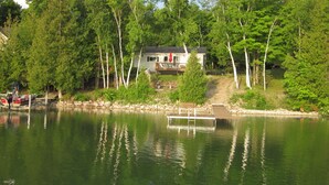 Un chalet au bord du lac, doté d’un quai, et entouré d’une forêt dense.
