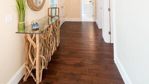 Un pasillo con piso de madera, una mesa con cubierta de vidrio y un candelabro único.