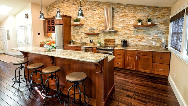 Una cocina con salpicadero de piedra, armarios de madera y una isla central con taburetes.