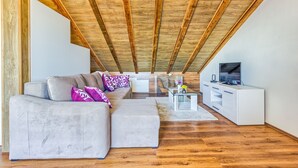 A modern loft with exposed wooden beams, a grey sectional sofa, a glass coffee table, and a white entertainment unit.