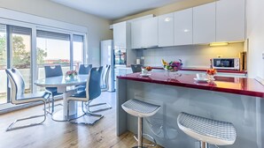 A modern kitchen with white cabinets, a red countertop, and a dining area with a glass table and metal chairs.